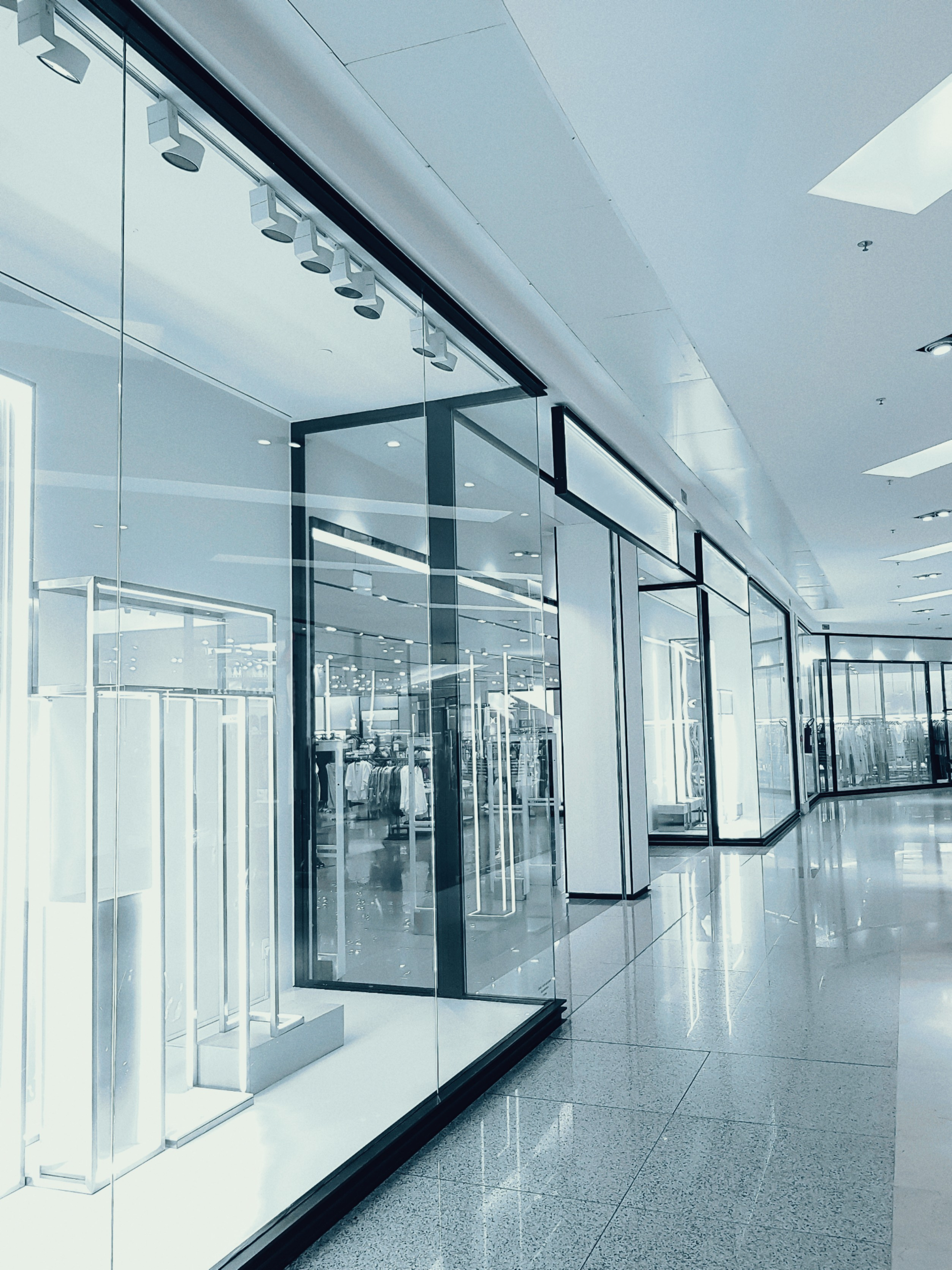 Bright and empty shopping mall corridor with glass display walls and reflections.